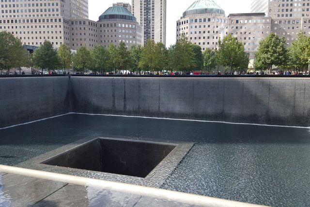 A photograph of one of two pools comprising the National September 11 Memorial, in lower Manhattan, with a crowd of tourists looking into the pool.